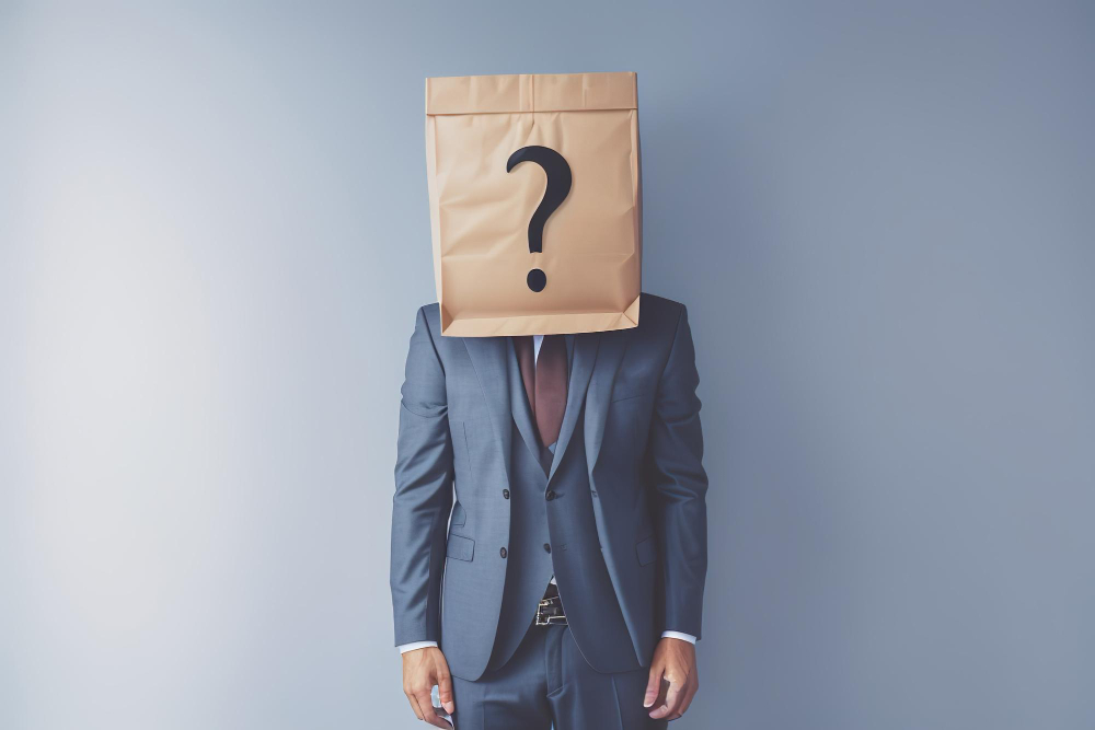 An image of a man in suit in a complete blank background covering its head with a paper bag with a question mark on it.